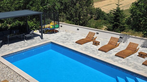 A swimming pool with lounge chairs and a covered seating area, surrounded by trees and a view of distant hills. - Charming Holiday home with private pool,teniss field WiFi... Imotski,Croatia (Gornji Vinjani)