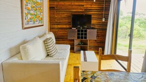Um quarto aconchegante com um sofá branco, um suporte de madeira para a TV e uma mesa.