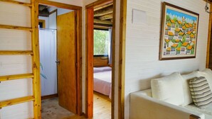 Quarto com escada de madeira, cama com manta rosa e sofá branco com almofadas listradas.