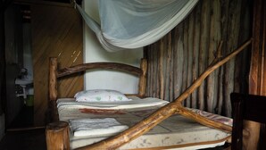 Un lit en bois rustique doté d’un baldaquin, une chaise en bois et une simple table de chevet.