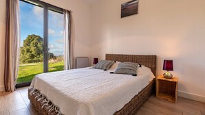Ein Schlafzimmer mit einem großen Bett, Blick auf eine grüne Landschaft und einem kleinen Nachttisch mit Lampe.