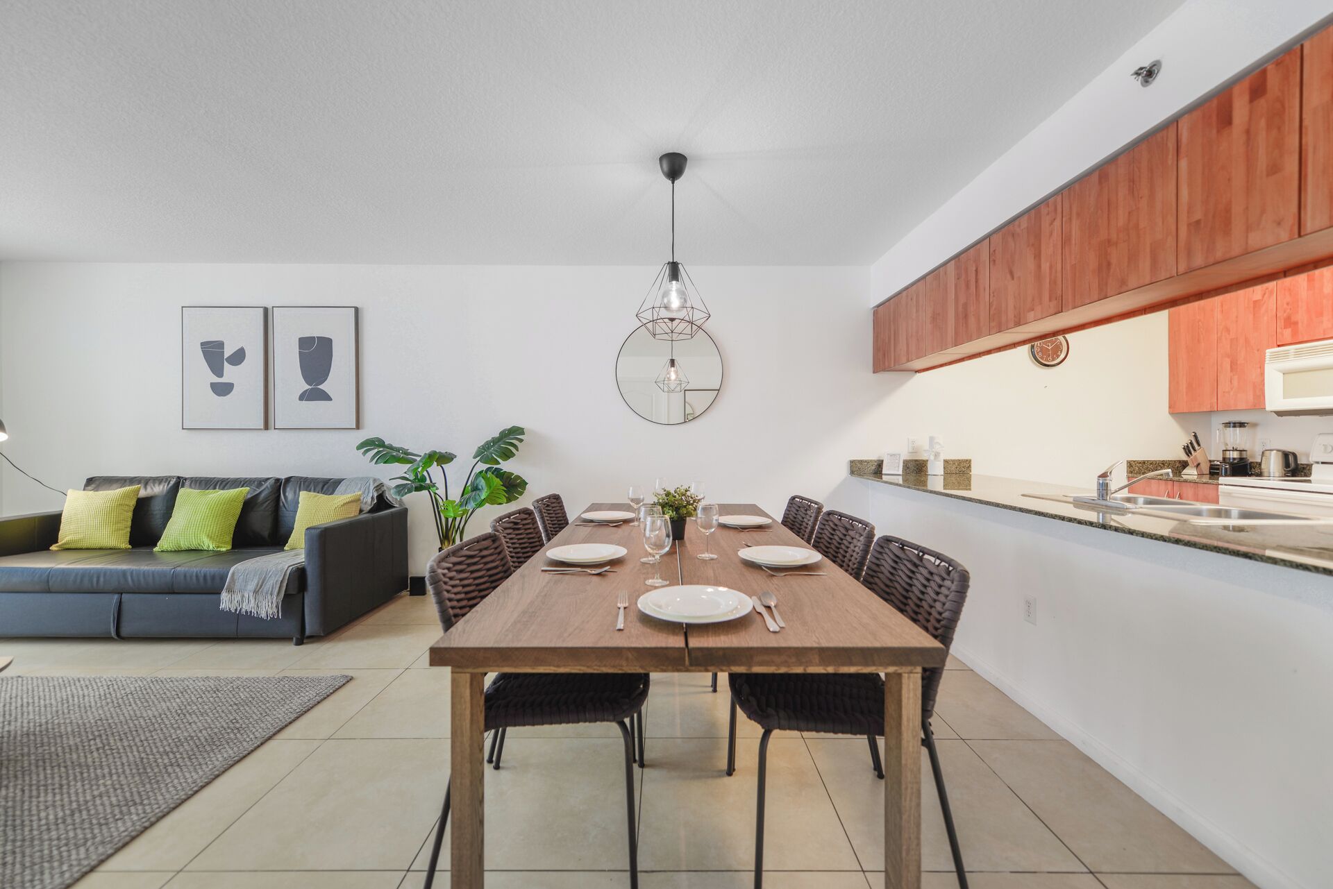 Una cocina moderna con armarios de madera, un comedor con mesa y sillas de madera, y una sala de estar con sofá y cojines.