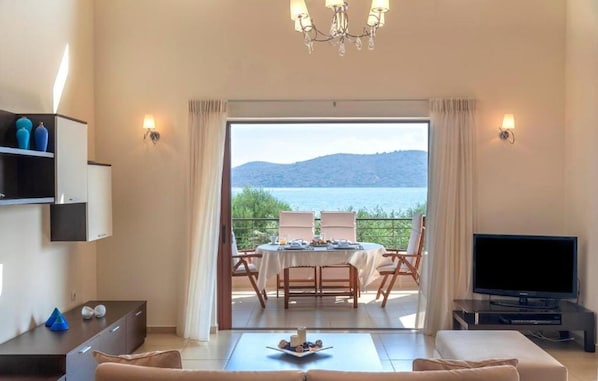 A living room with a TV, a dining table with chairs, and a view of a lake.