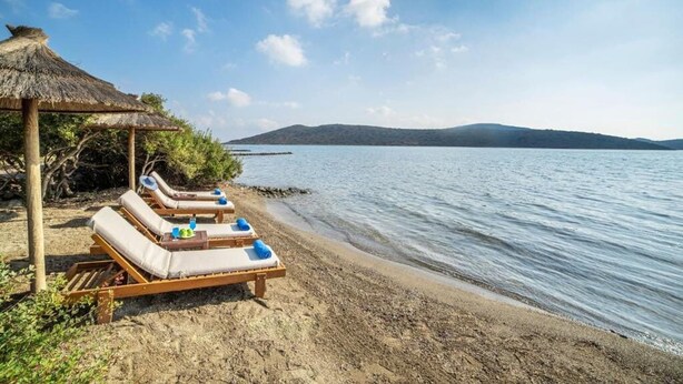 A beach with sun loungers and a thatched structure. - Elounda Blue Island Villa (Agios Nikolaos)