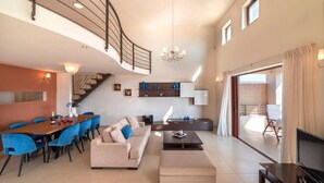 A spacious living area with a staircase, a dining table with chairs, a sofa, a coffee table, and a television. - Elounda Blue Island Villa (Agios Nikolaos)