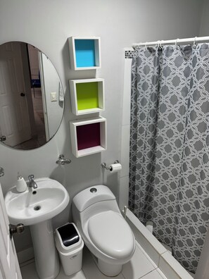 Bathroom features a pedestal sink, toilet with foot pedal, and shower area with a patterned curtain.