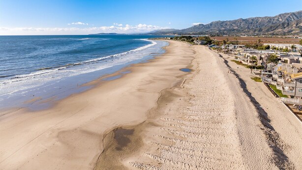 Une plage bordée de maisons mobiles, un ciel dégagé et des montagnes en arrière-plan.