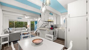 Une cuisine moderne avec des meubles blancs, une bouilloire rouge et une fenêtre à cadre bleu.