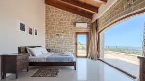 A bedroom with a stone wall, a bed, a nightstand, a window with a view, and a door. - Arios Lux villa,50 sqm pool,Rural,8 guests,Rethymno (Agia Paraskevi)