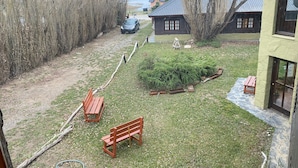 A grassy area with wooden benches, a small garden, and a building with a metal roof. - Kalenshen Calafate (El Calafate)