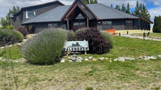 A log cabin with a metal roof and a mountain silhouette sign in front. - Kalenshen Calafate (El Calafate)