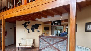 A reception area with a wooden reception desk, a world map on the wall, and a sofa. - Kalenshen Calafate (El Calafate)