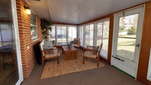A sunroom with a brick wall, large windows, and a seating area with a table and chairs. - Timo's Place (Wilmington)