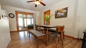 A dining area with a wooden table, four chairs, a bench, a ceiling fan, a clock, a plant, and a painting on the wall. - Timo's Place (Wilmington)