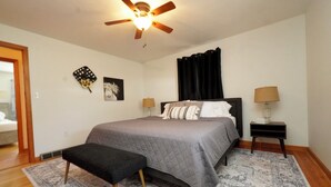 A bedroom with a bed, two bedside tables with lamps, a ceiling fan, a black bench, and a patterned rug. - Timo's Place (Wilmington)