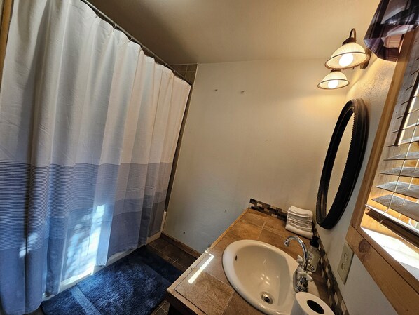 A bathroom with a shower curtain, a sink, a mirror, and a towel rack.
