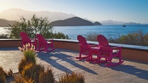 A terrace with four rocking chairs overlooking a body of water with mountains in the background. - 2 bed, 3 bath, full kitchen, in-room laundry, balcony at tranquil golf resort  (Ensenada Blanca)