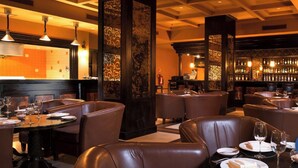 Een restaurant met leren zitbanken, een bar met flessen en een keuken op de achtergrond.
