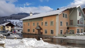 Un bâtiment à deux étages, dont le toit est recouvert de neige, avec une entrée bien visible et une enseigne indiquant « Hôtel ».