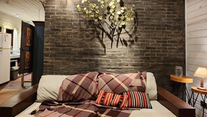 Un salón acogedor con techo de madera, pared decorativa de ladrillo y sofá con manta escocesa.