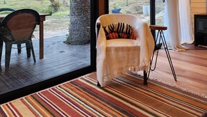 Una habitación acogedora con un amplio ventanal corredera que da a una terraza exterior, un sillón cómodo, una mesita y un televisor.