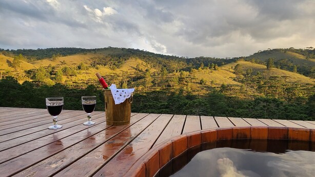 Una terraza de madera con dos copas de vino tinto y un candelabro, con vistas a un paisaje montañoso.