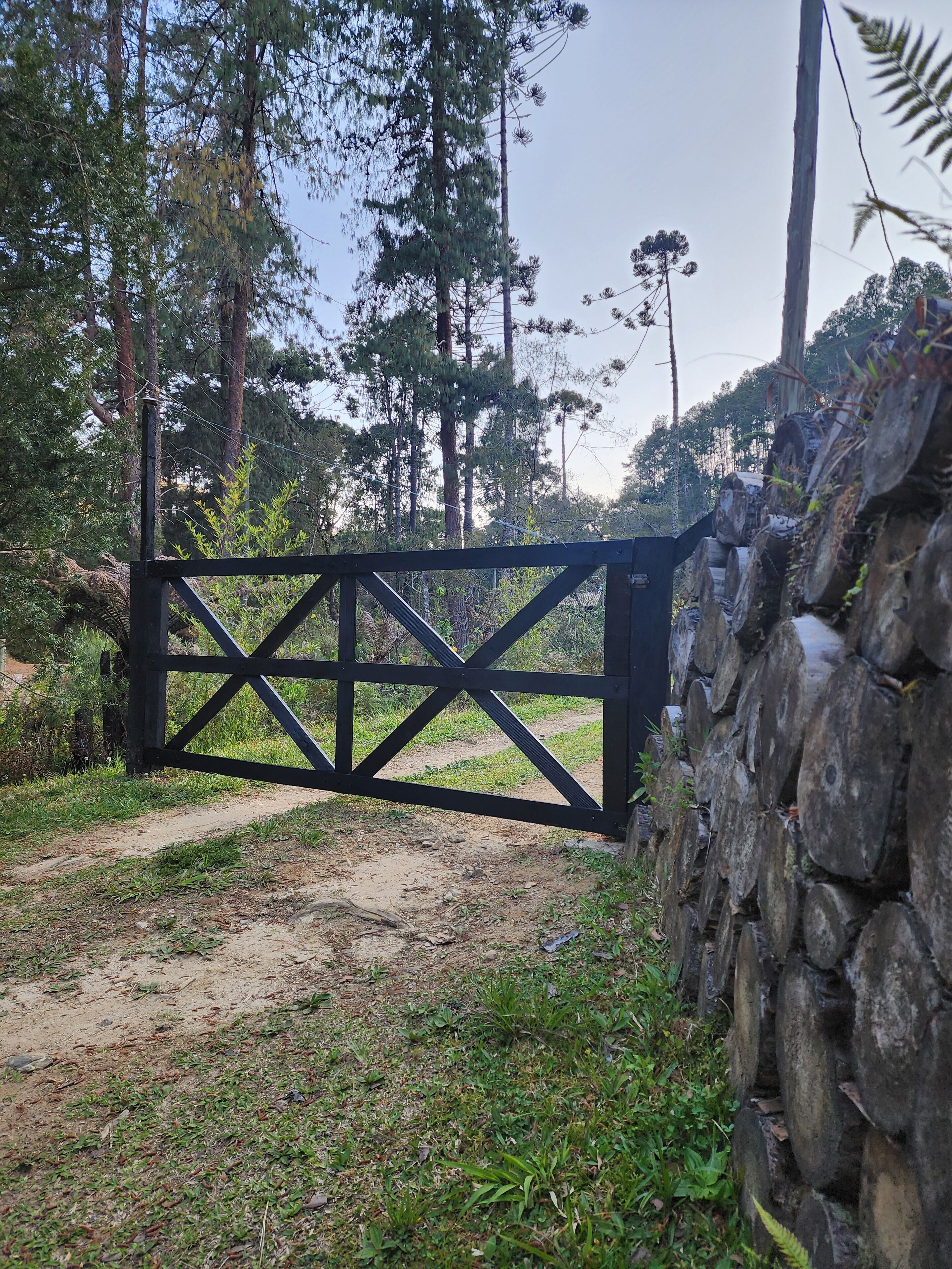 A gated entrance with a stone wall on one side and a dirt path leading through.