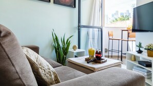 A modern living room with a sofa, a coffee table with snacks, a TV, and a view of the city through a large window. - Piscina - Ibirapuera - Brazillian Corner (São Paulo)