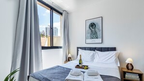 A hotel room with a bed, a window with curtains, a framed picture on the wall, a bedside table with a lamp, and a nightstand with books. - Piscina - Ibirapuera - Brazillian Corner (São Paulo)
