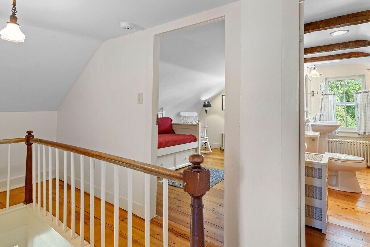 A staircase with wooden railings and a white banister leading to a bedroom with a red bedspread.