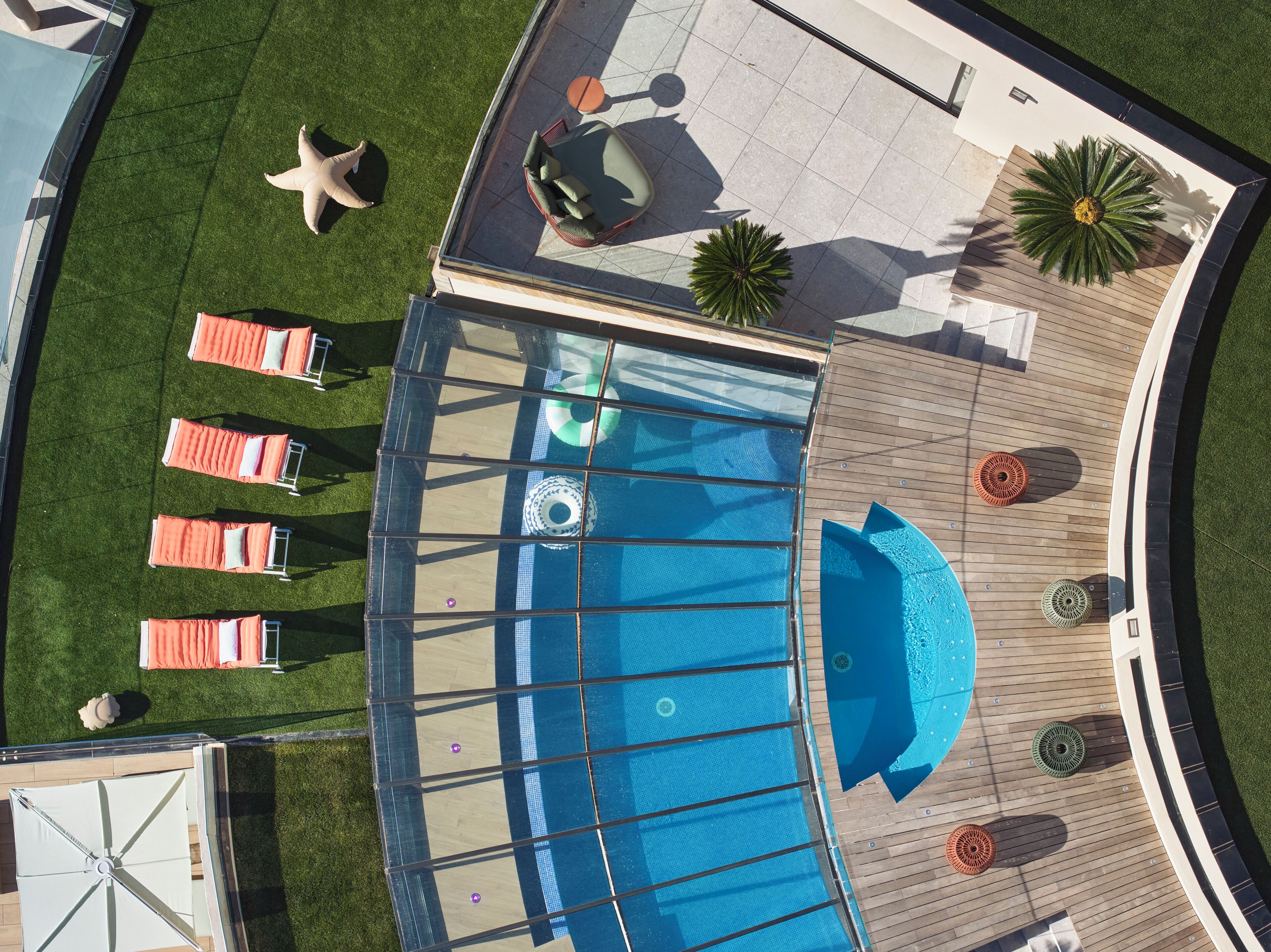 An aerial view of a rooftop pool area with lounge chairs, a sun lounger, and a palm tree.