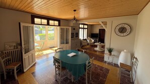 A dining area with a wooden ceiling, a round table with chairs, a clock on the wall, and a view through the open door. - Family home 300m from the beach  (Saint-Jean-de-Monts)