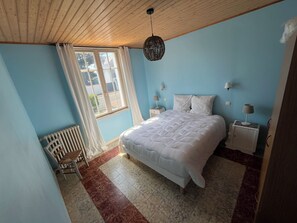 Een slaapkamer met een bed, nachtkastje, lamp, stoel, radiator en een raam met gordijnen.