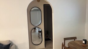 Een eetgedeelte met een houten tafel en stoelen, een kleine ronde tafel met een kaars, en een spiegel aan de muur.