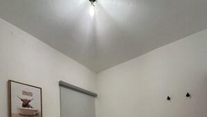 Een net opgemaakt bed met witte lakens, een ingelijst foto aan de muur en een plafondlamp.
