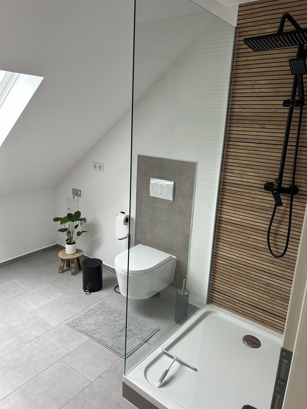 A modern bathroom with a freestanding bathtub, a showerhead, a toilet, and a small potted plant. - Beautiful, newly renovated vacation apartment (Spalt)