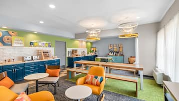 Eine moderne Küche mit blauen Schränken, ein Essbereich mit einem Holztisch und orangefarbenen Stühlen sowie ein grüner Teppich.