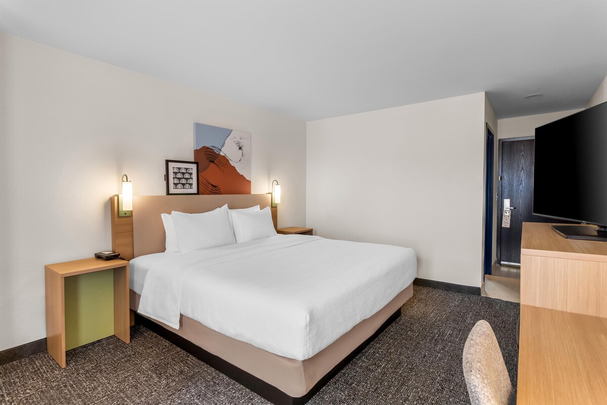 Habitación de hotel con cama, mesitas de noche, televisor y cuadros en la pared.