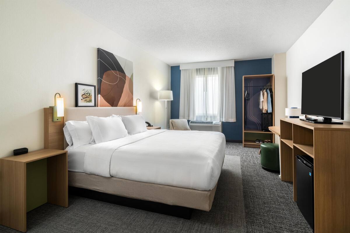 A hotel room with a large bed, bedside tables, a TV, a wardrobe, and a window with curtains.