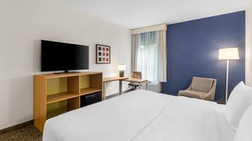 Habitación de hotel con cama, escritorio, silla, televisión y ventana con cortinas.