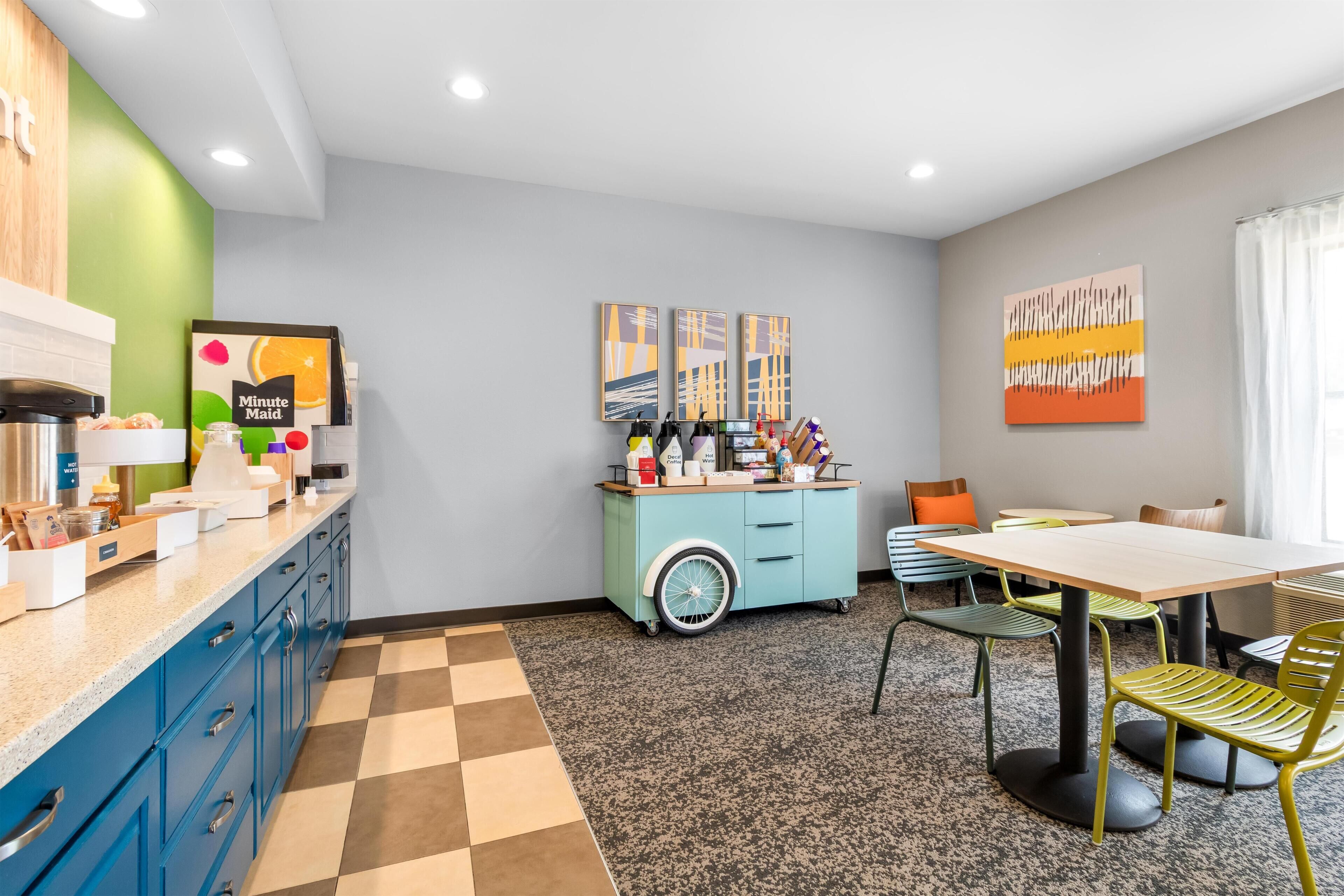 Una cocina moderna con una estación de café, un comedor con mesa y sillas, y obras de arte en las paredes.