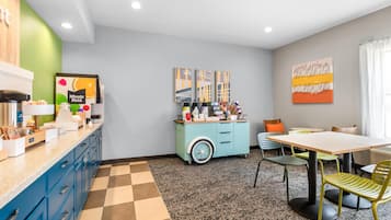 Una cocina moderna con una estación de café, un comedor con mesa y sillas, y obras de arte en las paredes.