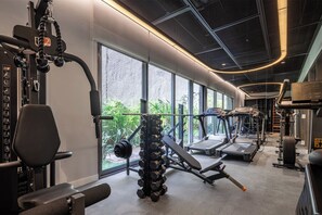 Un gimnasio moderno con diversos equipos de ejercicio, amplias ventanas y vistas al exterior con zonas verdes.