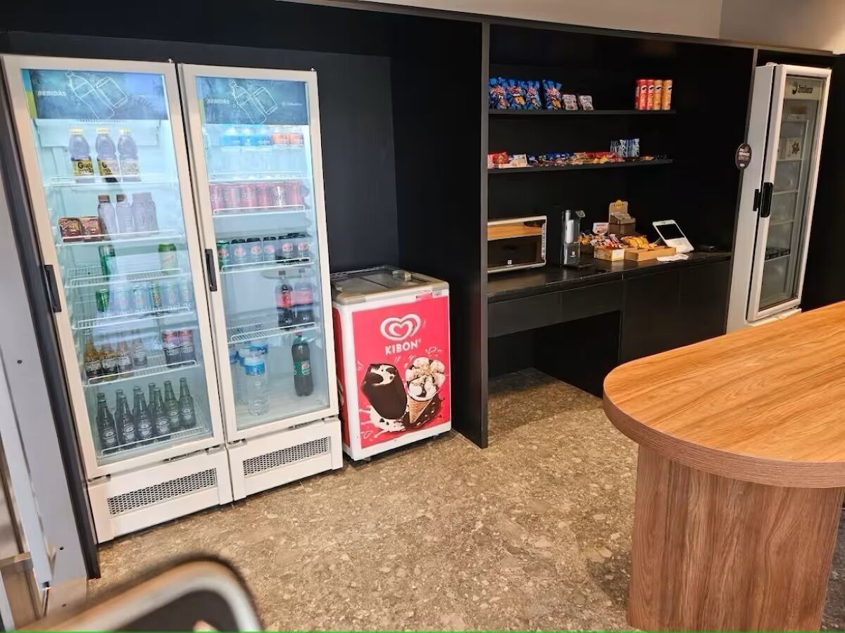 Un espace de vente proposant deux distributeurs automatiques de boissons réfrigérées, un petit réfrigérateur orné d’une publicité pour les glaces Kibon, ainsi que des étagères remplies de collations et de boissons.