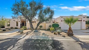 A residential building with a garage, a driveway, and desert landscaping including cacti and a palm tree.