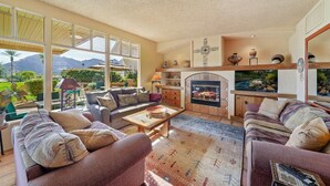 A spacious living room with large windows, a fireplace, and a view of mountains.