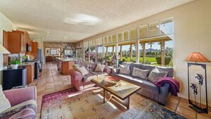 A spacious living area with a sofa, coffee table, and a view of a garden through large windows.