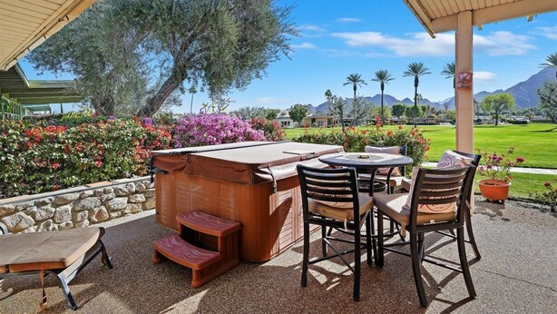 A covered outdoor patio with a hot tub, seating area, and a stone wall.