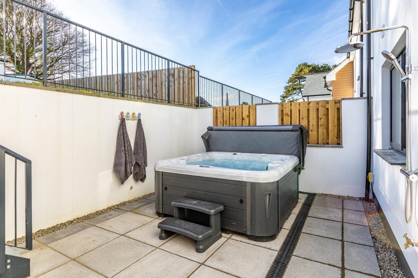 A hot tub with a step stool, a wooden fence, and a metal railing in a backyard.