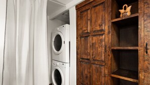 A laundry room with two stacked washing machines and a wooden cabinet with shelves. - Native Charm Adobe Guesthouse in Historic Old Town with wifi, AC, patio grill. (albuquerque)